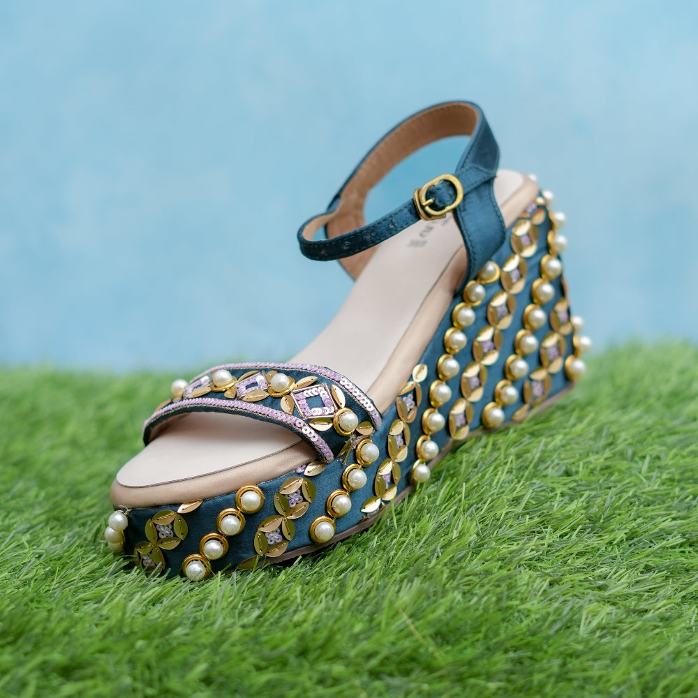 Blue sandal with gold embellishments on a grassy surface