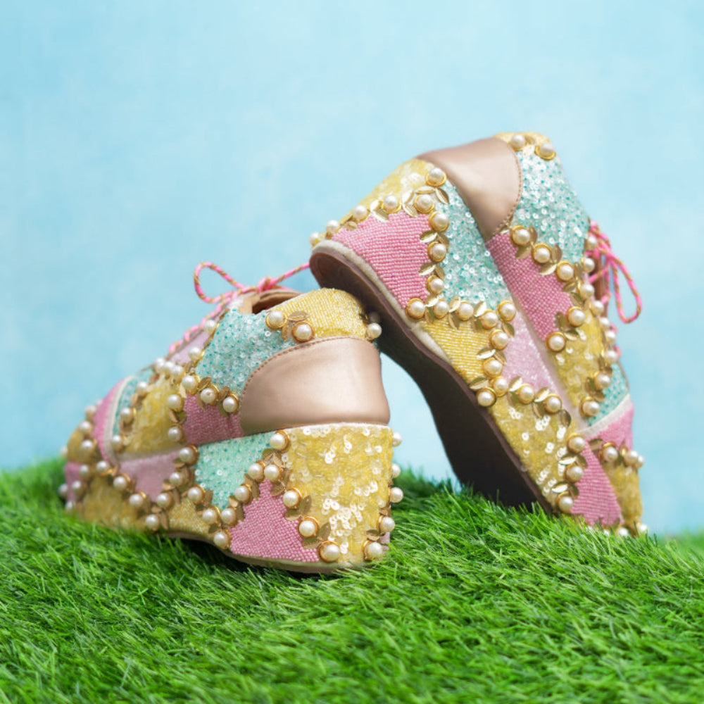 Colorful high-heeled shoes with pearl embellishments on a grassy surface.
