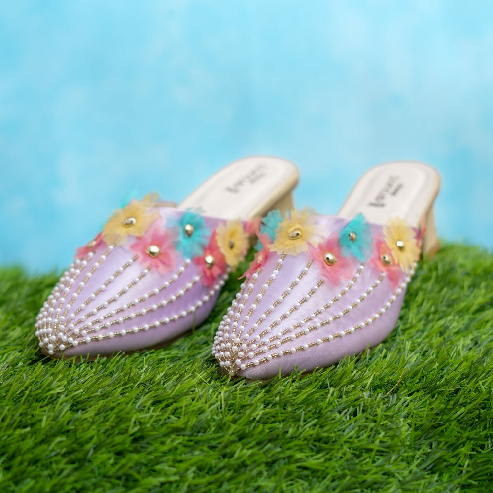 Decorative shoes with flowers and pearls on a grassy surface with a blue sky background