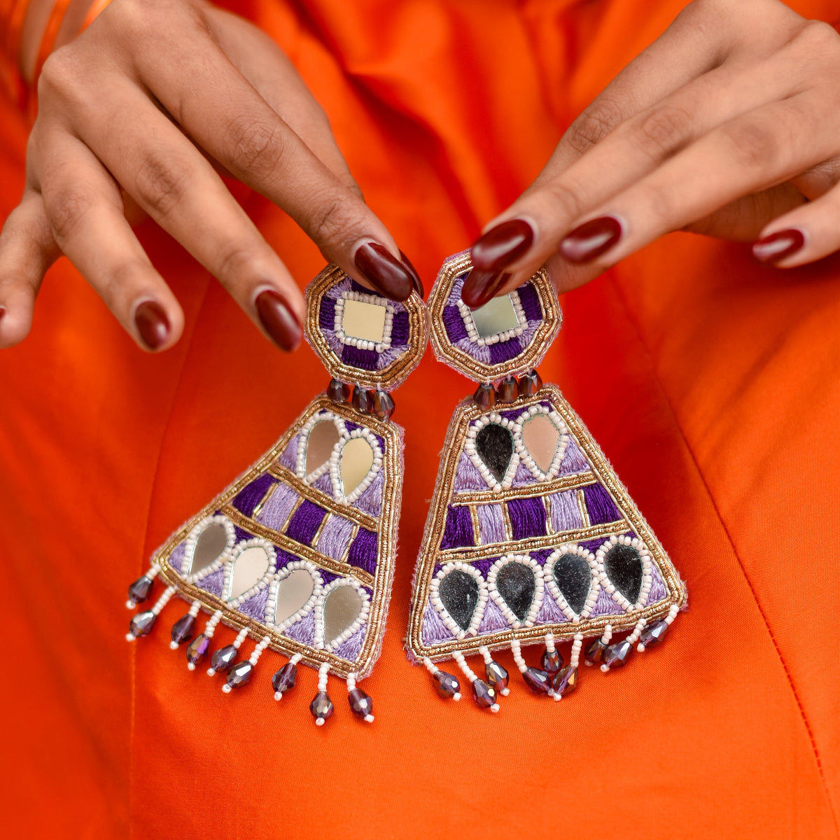 Colorful beaded earrings held by a bride against an orange outfit