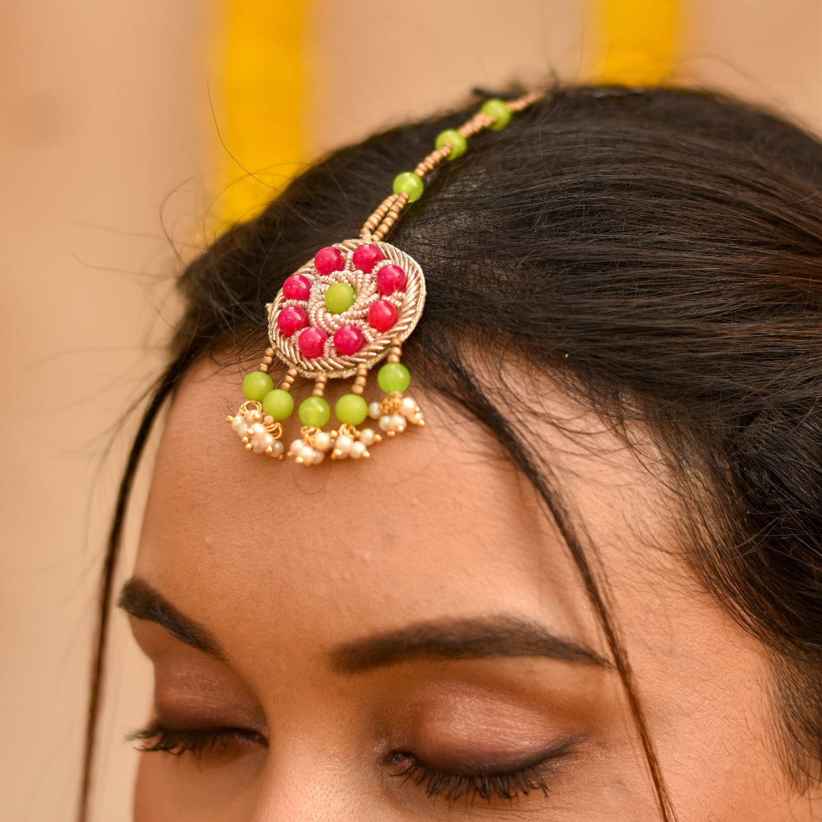 A bride wearing a beaded maangtika featuring green and red beads for haldi
