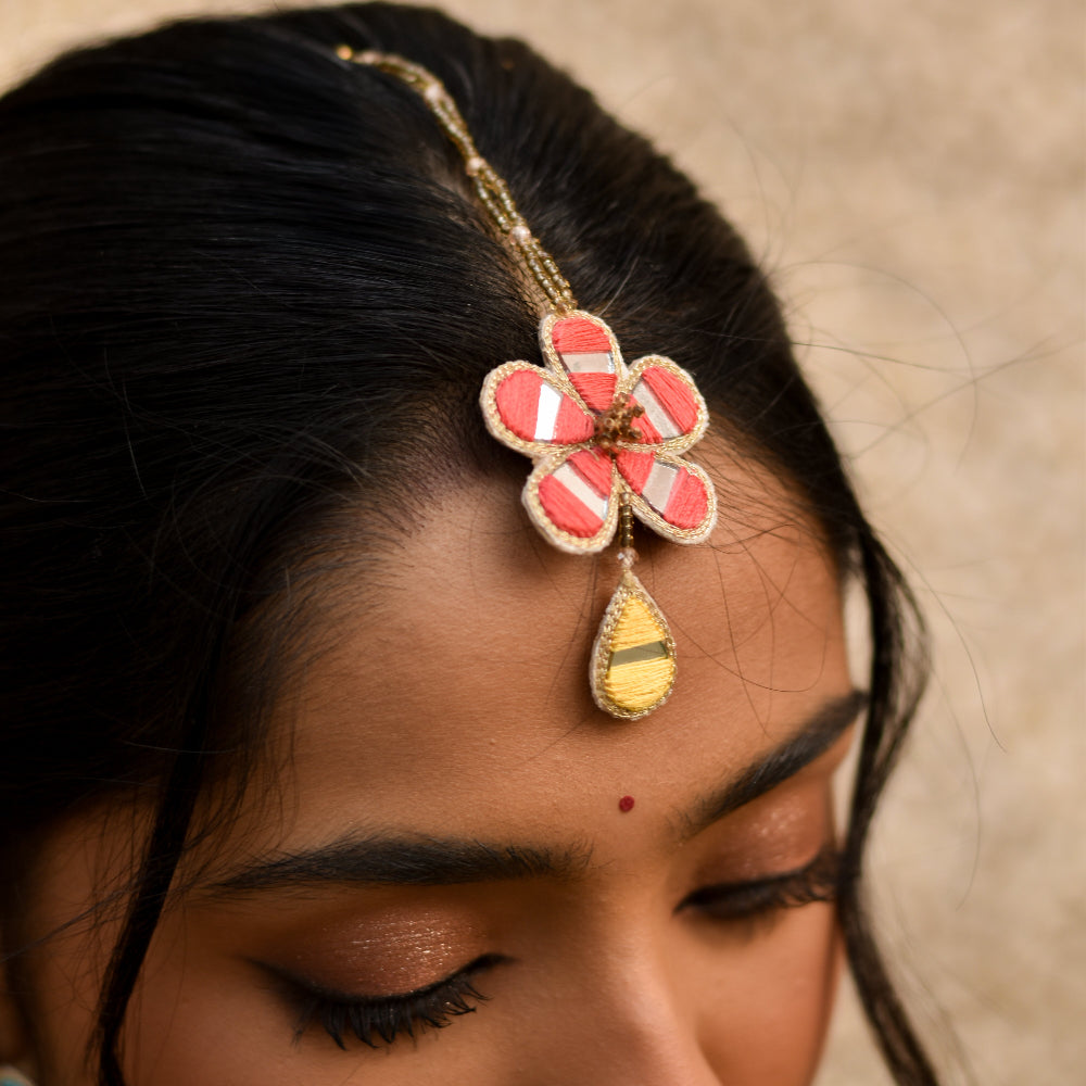 Bride wearing a decorative headpiece maangtika in a pink flower design for her haldi look