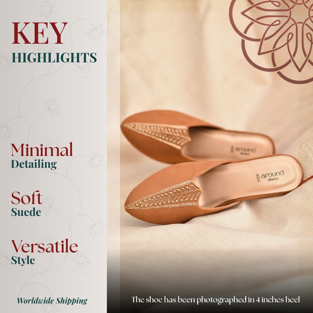 Refined soft tan mules with subtle stitched patterns and a pointed toe finish, styled on a neutral fabric backdrop.
