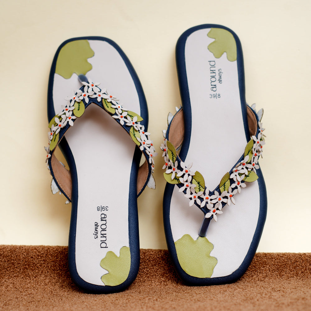 Blue sandal featuring white flower appliqués and green leaf shapes

