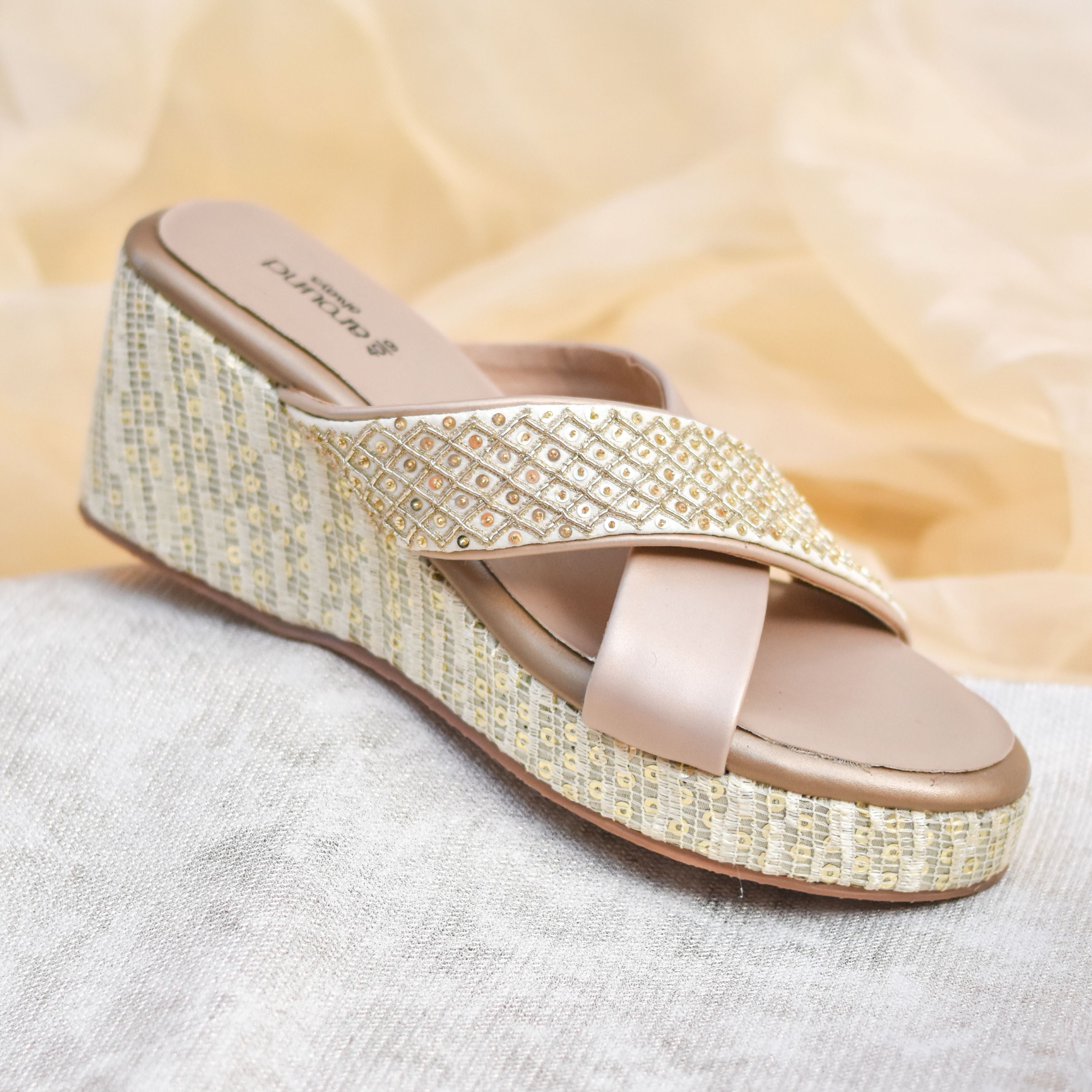 Beige and gold slip-on wedge sandals with embellished crisscross straps.