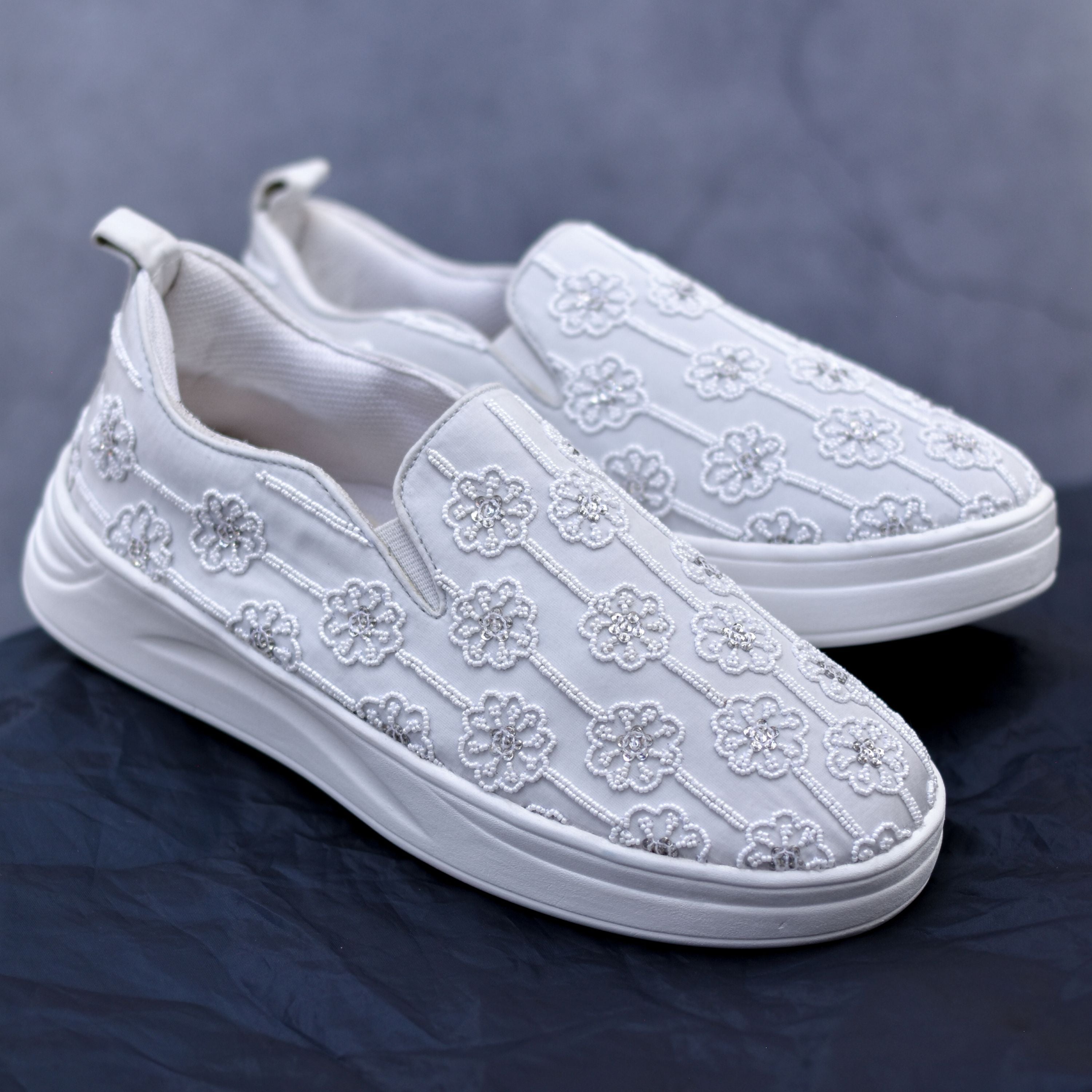 White slip-on sneakers with floral beadwork and cushioned sole.
