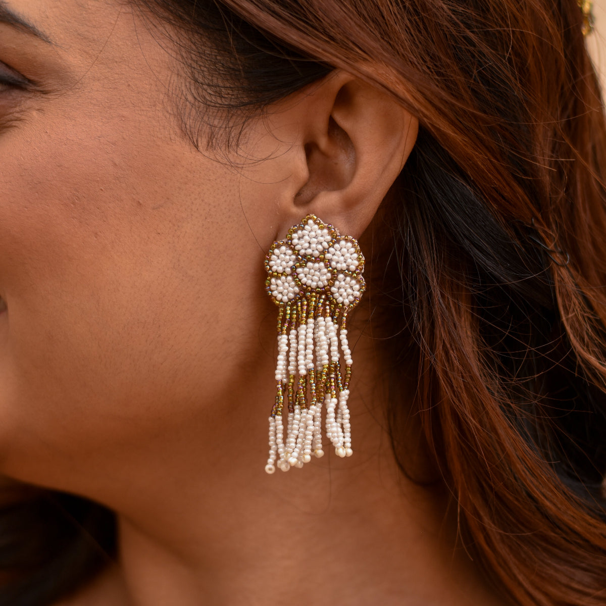 An Indian girl wearing a beaded golden and white earrings with long drops 