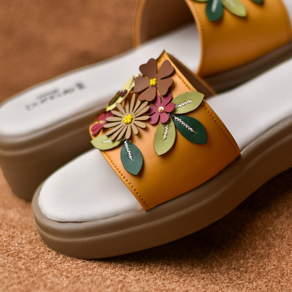 Mustard slip-on slides decorated with layered blossoms and leaf appliqués