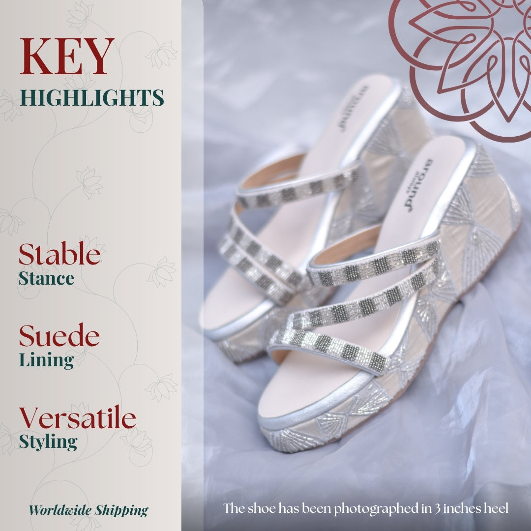 Silver wedge sandals with crisscross straps, textured embroidery, and cushioned sole, styled on soft fabric backdrop for elegant festive wear.