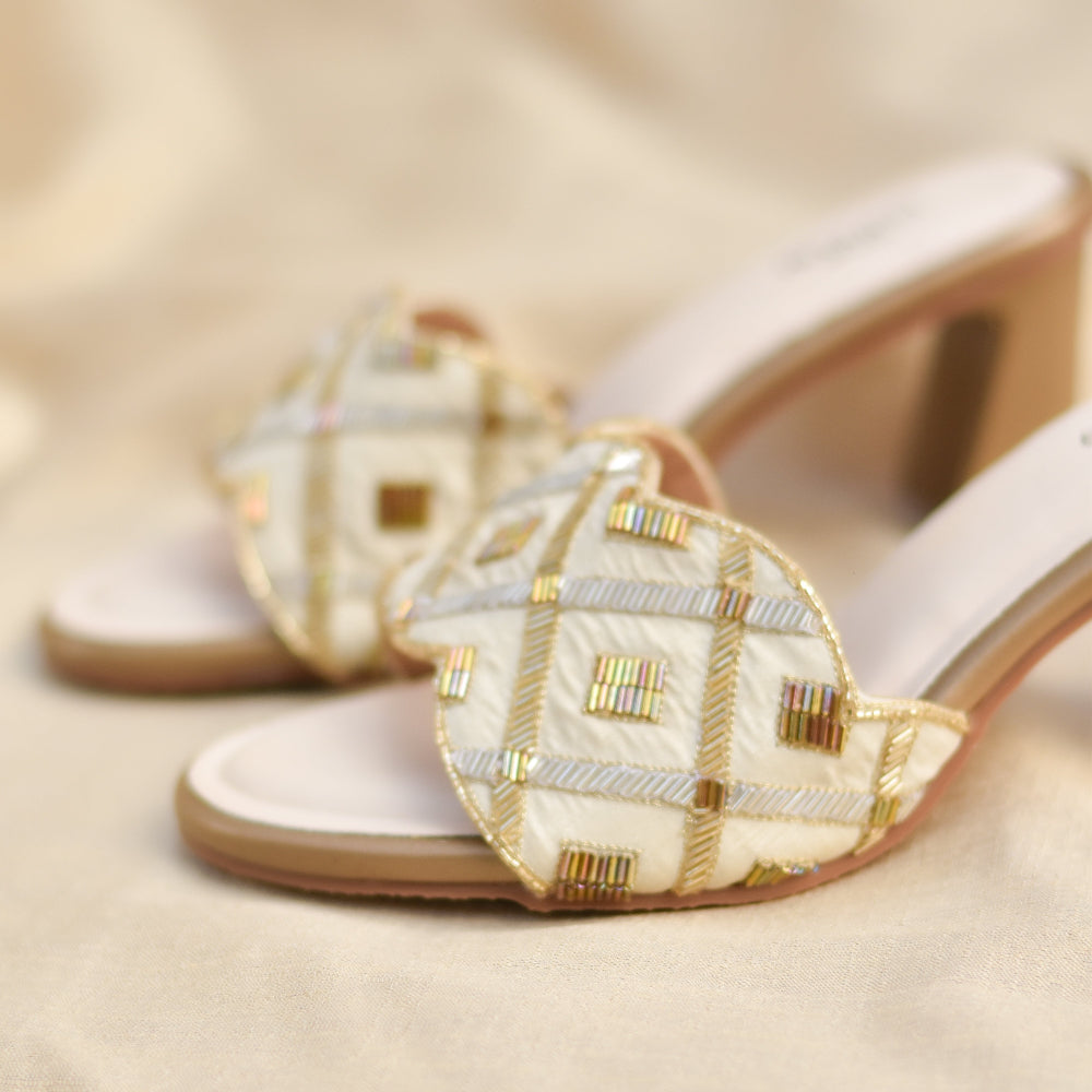 Gold flared heel footwear with geometric pattern on ivory base.