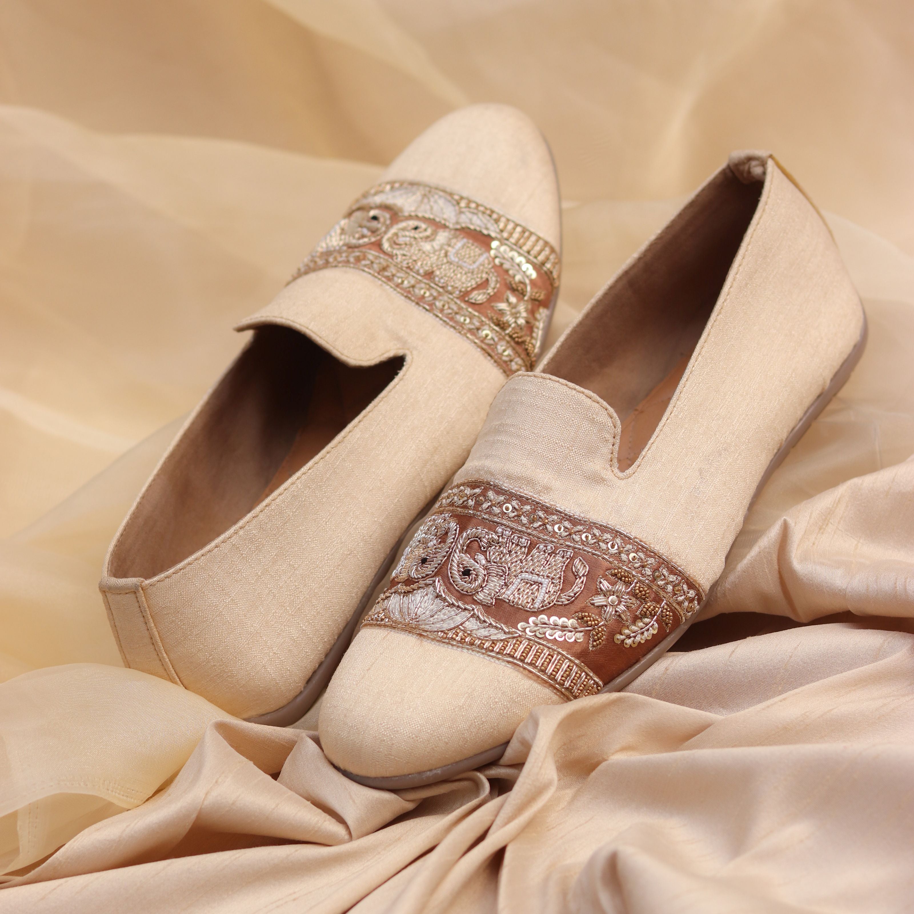 Luxury beige shoes with bold embroidered band showcasing traditional motifs.