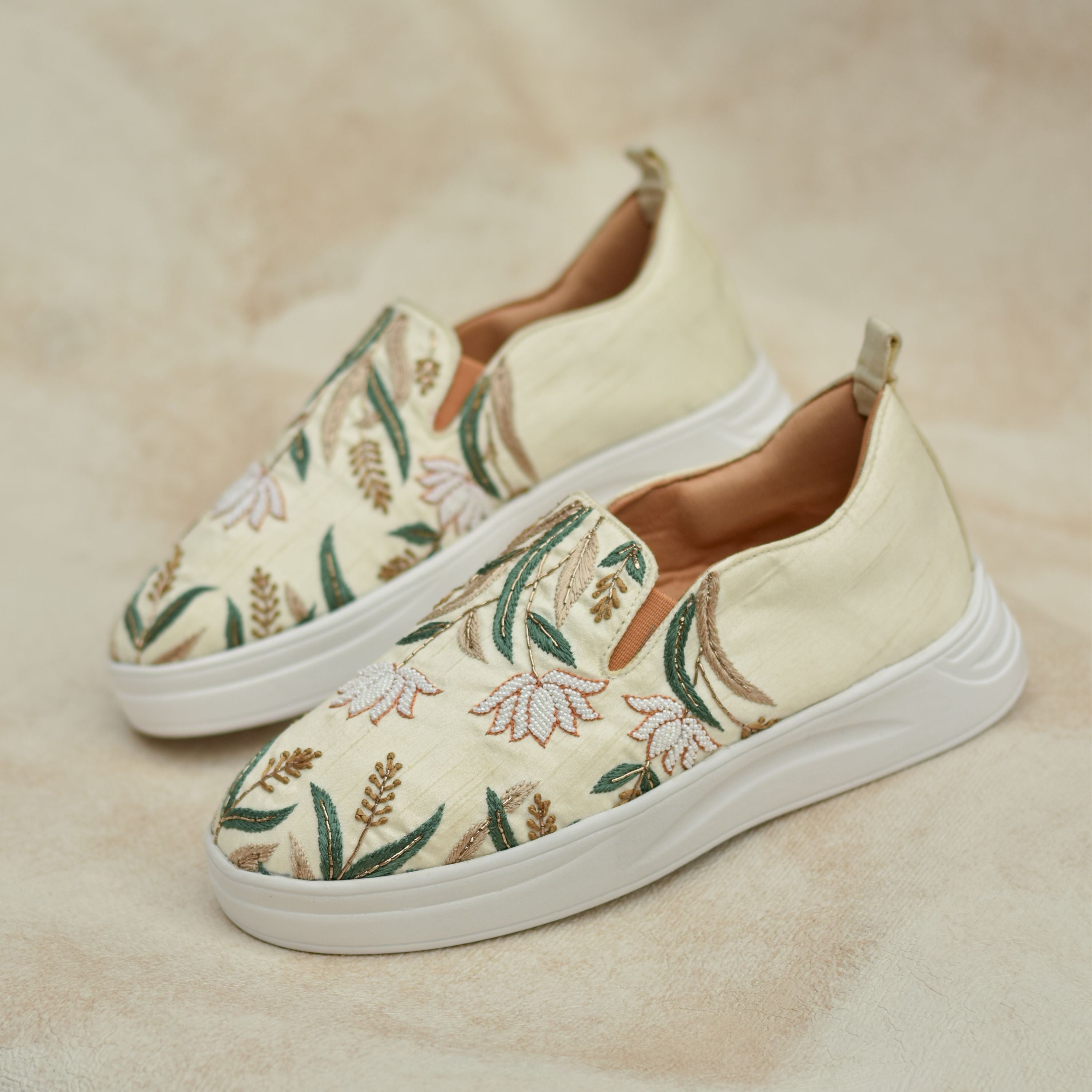 Beige slip-on sneakers with green leafy embroidery and white floral beadwork.