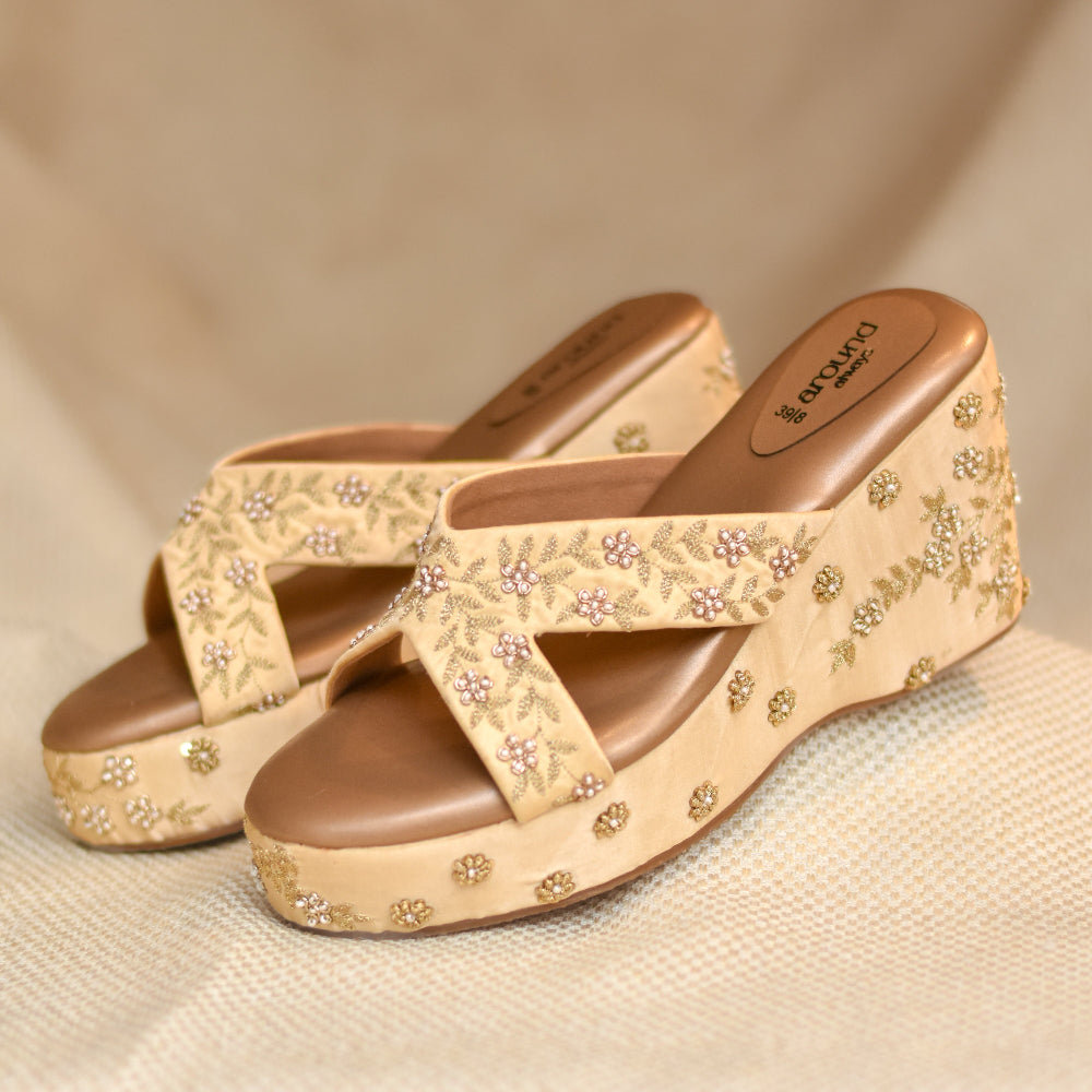 Golden crossover wedge sandals with floral vine embroidery and pearl detailing
