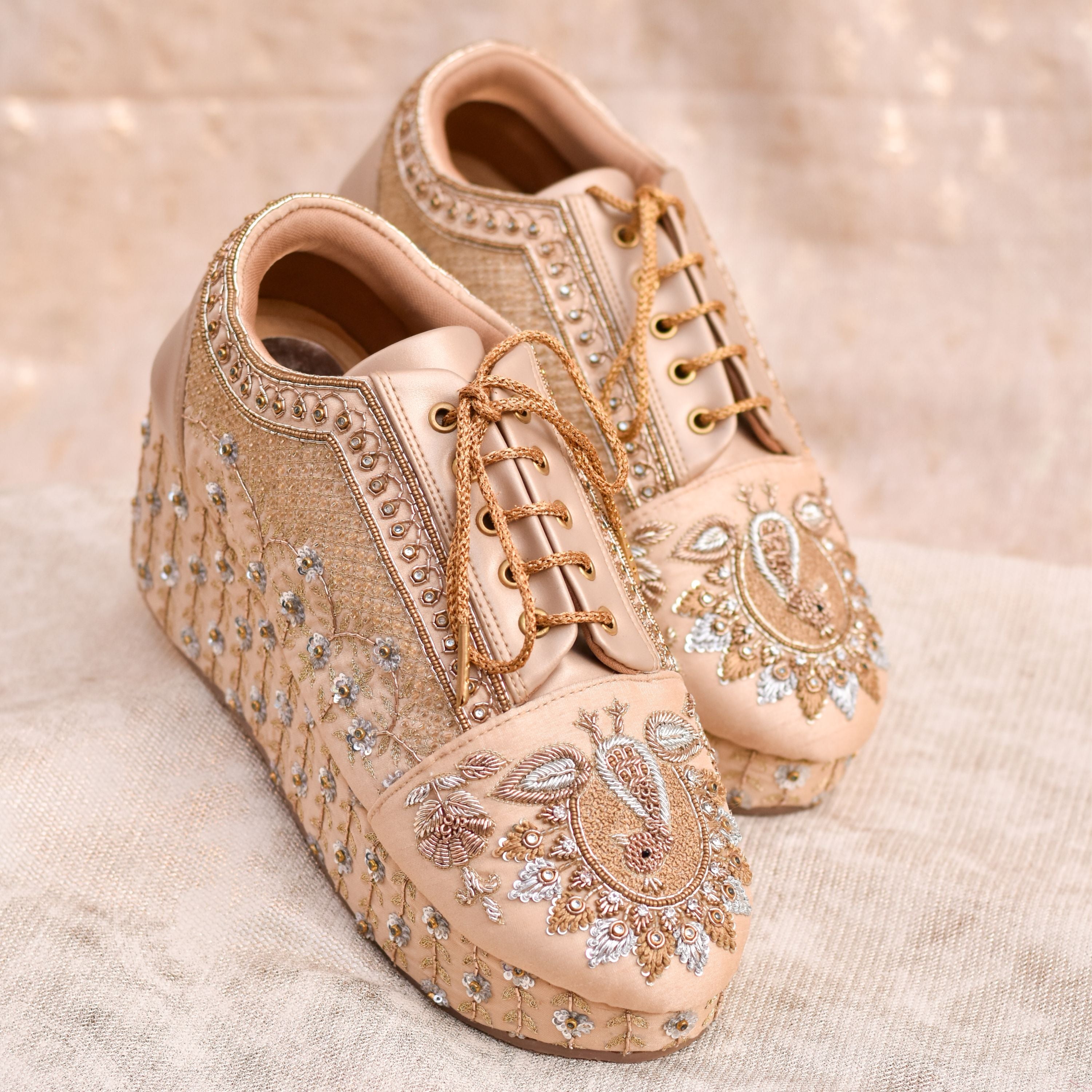 Gold wedge sneakers with floral beadwork and lace-up design.