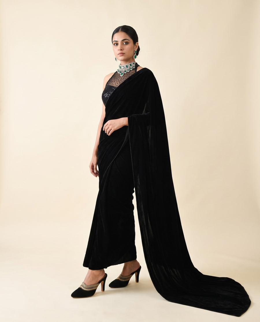 An Indian woman wearing black velvet saree paired with designer Indian mules with golden detailing 
