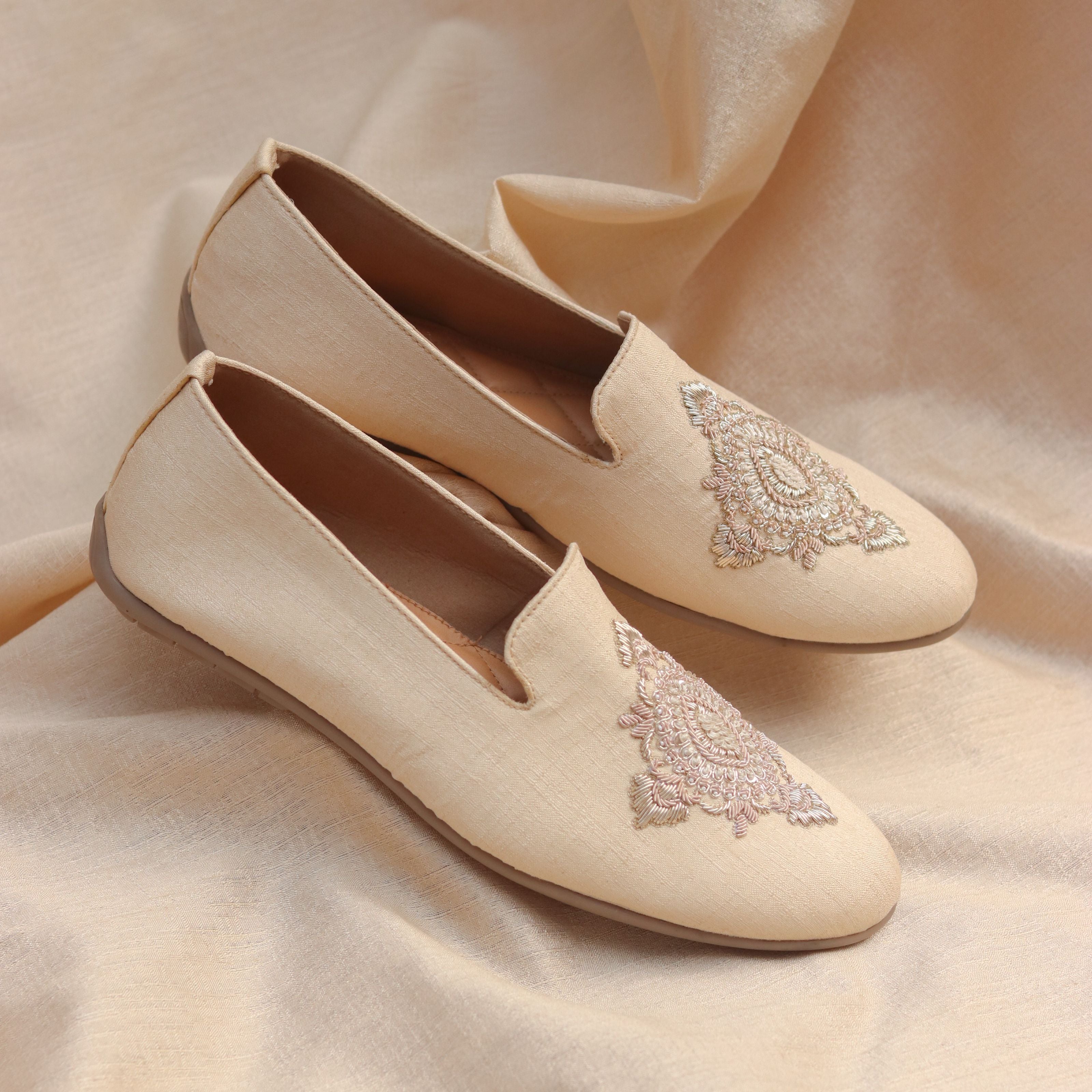 Soft beige slip-on shoes with subtle sheen and delicate floral embroidery.