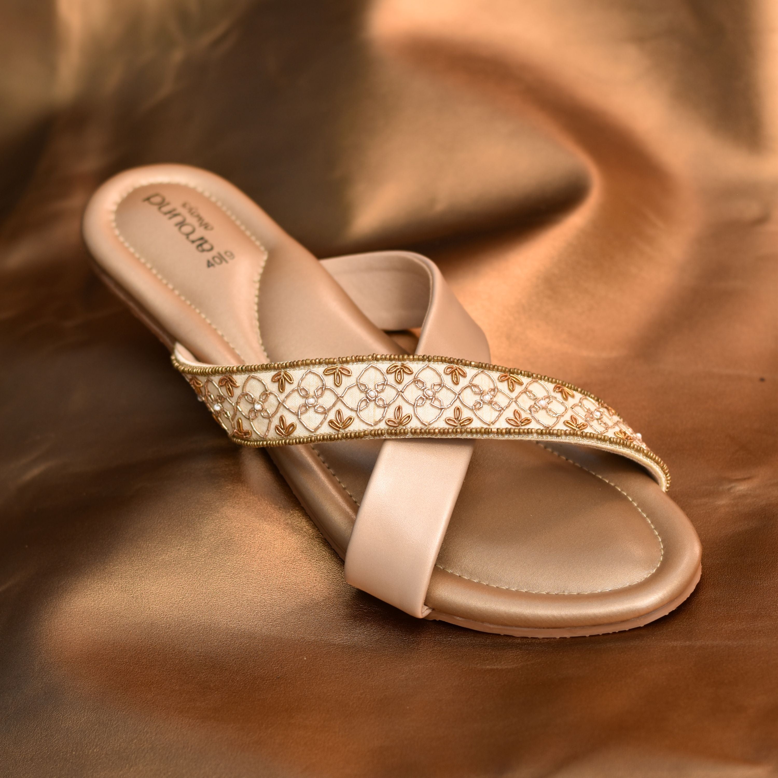 Beige crossover flats with white and gold embroidered strap.