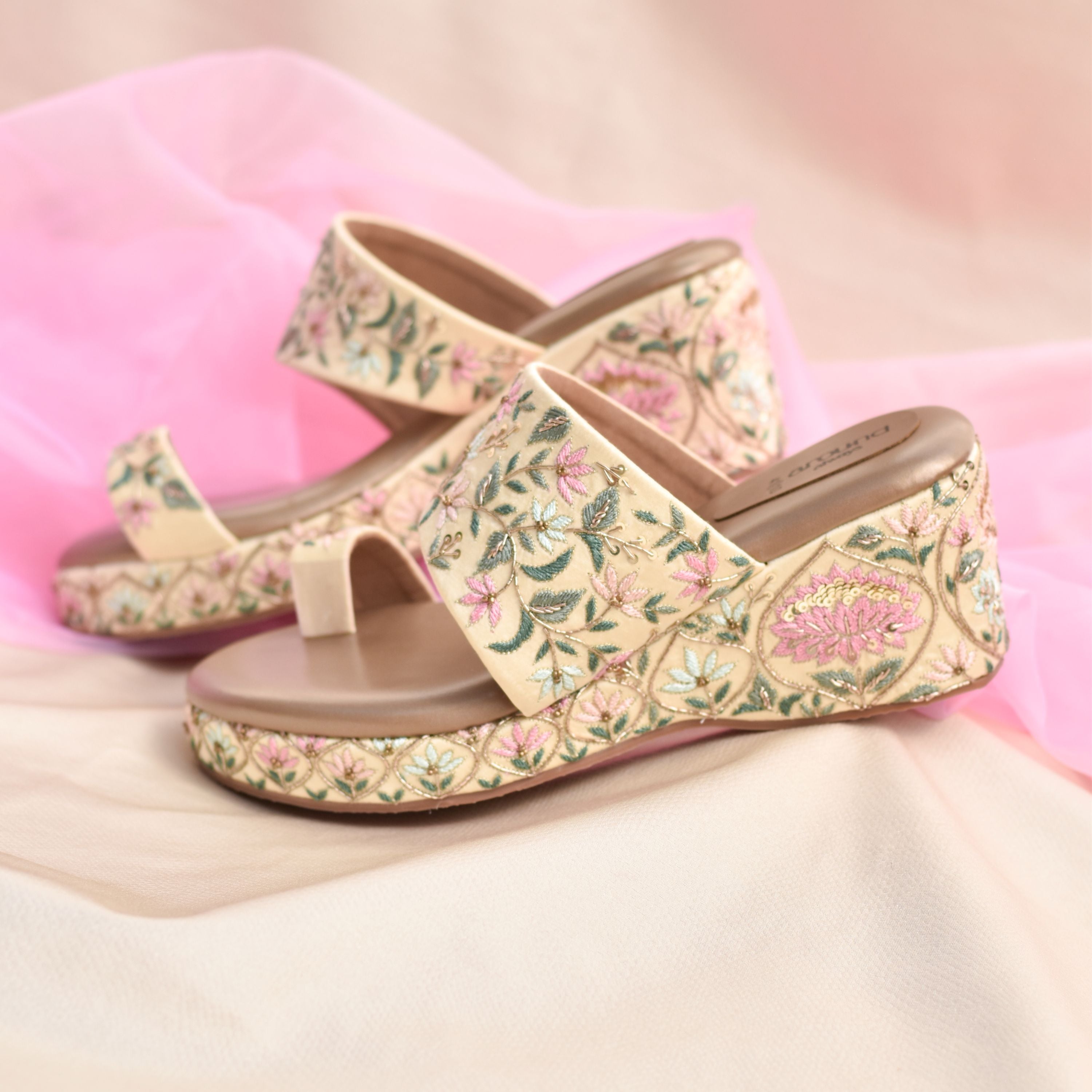 Beige gold wedge sandals with pastel floral threadwork on strap and heel.
