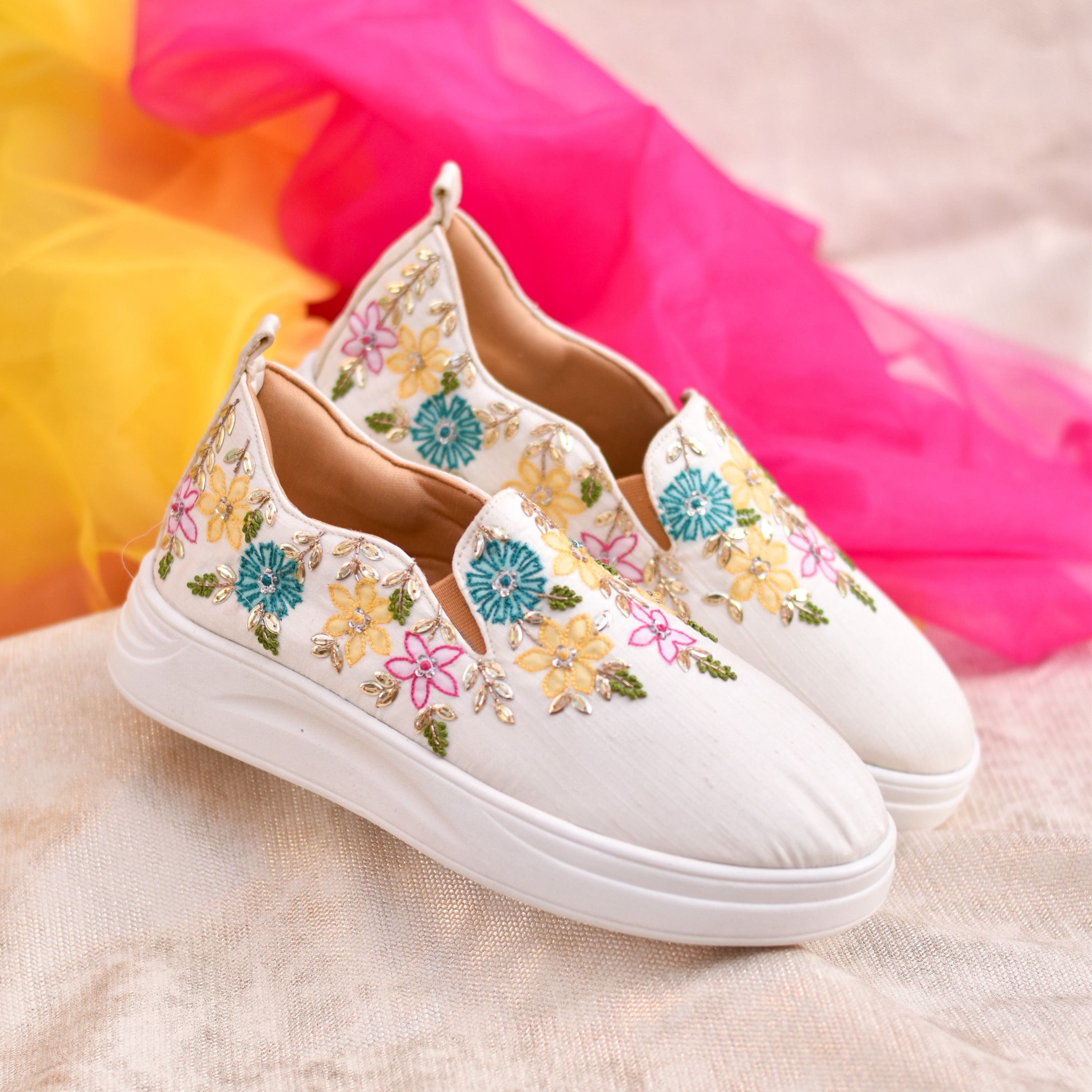 White slip-on sneakers with colorful floral embroidery and cushioned sole.