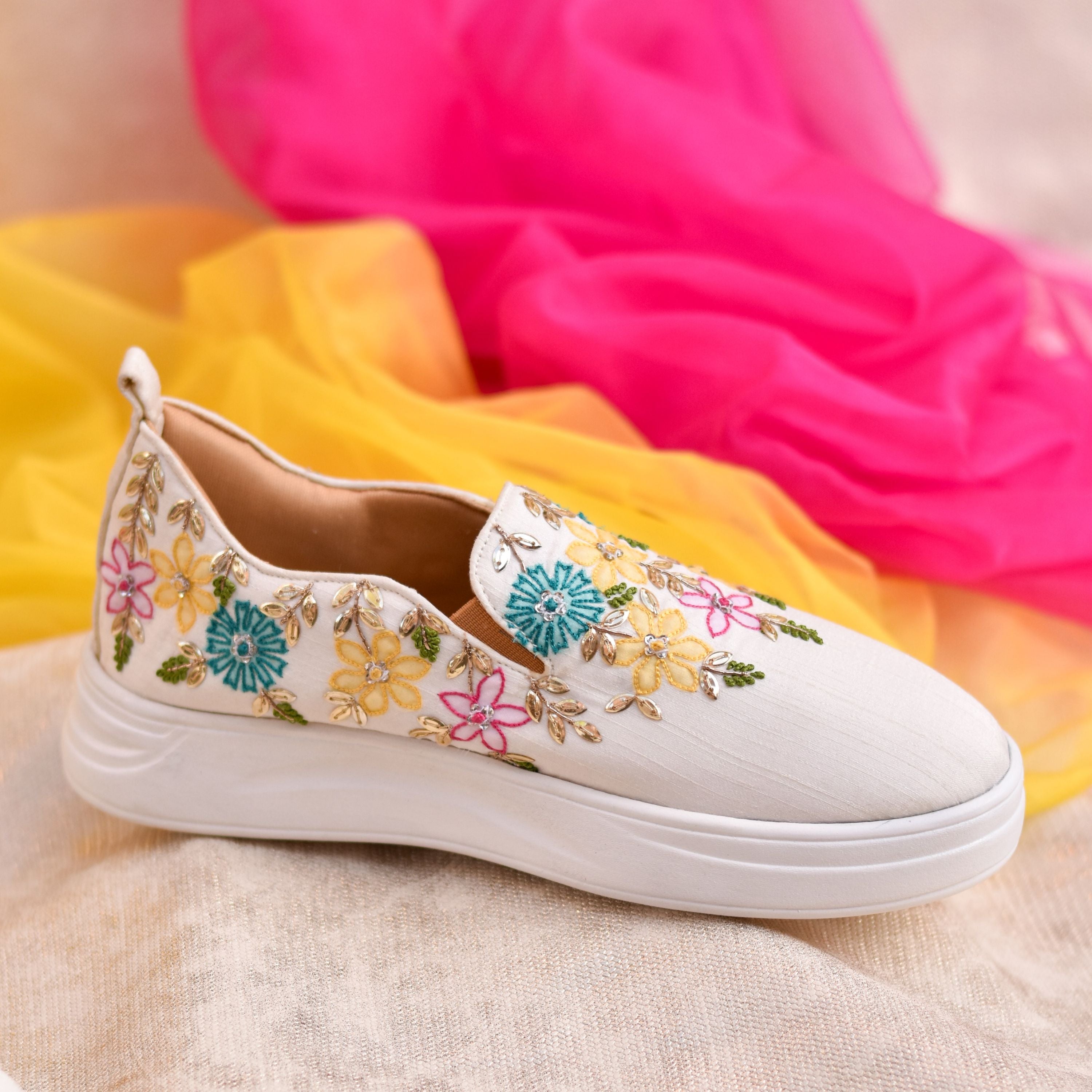 Women’s slip-on shoes with multicolor floral handwork on white base.