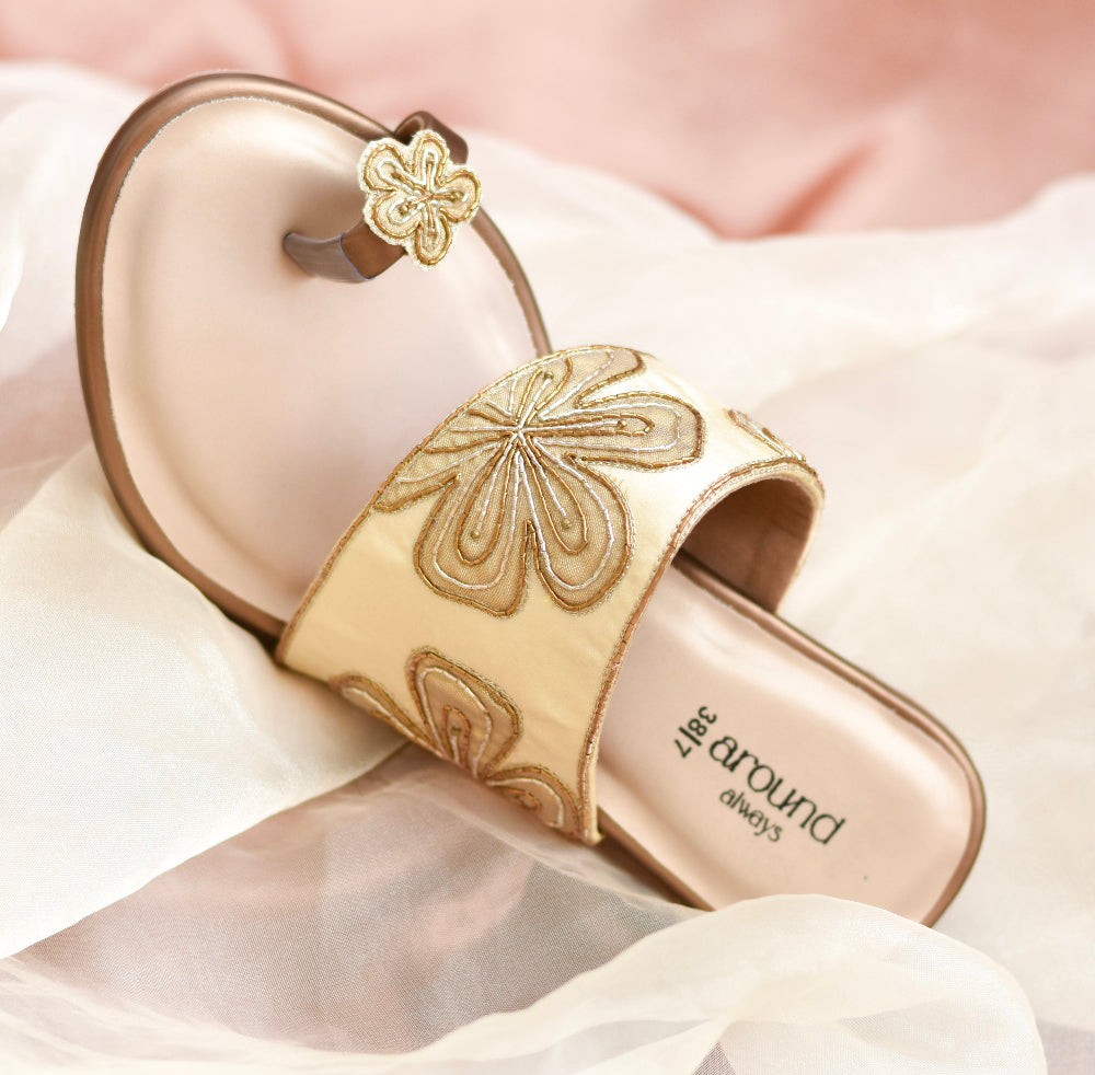 Designer gold strap heel with floral-inspired toe motif resting on cushioned insole
