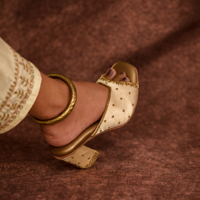 Gold high-heeled shoe styled with neutral ivory pants