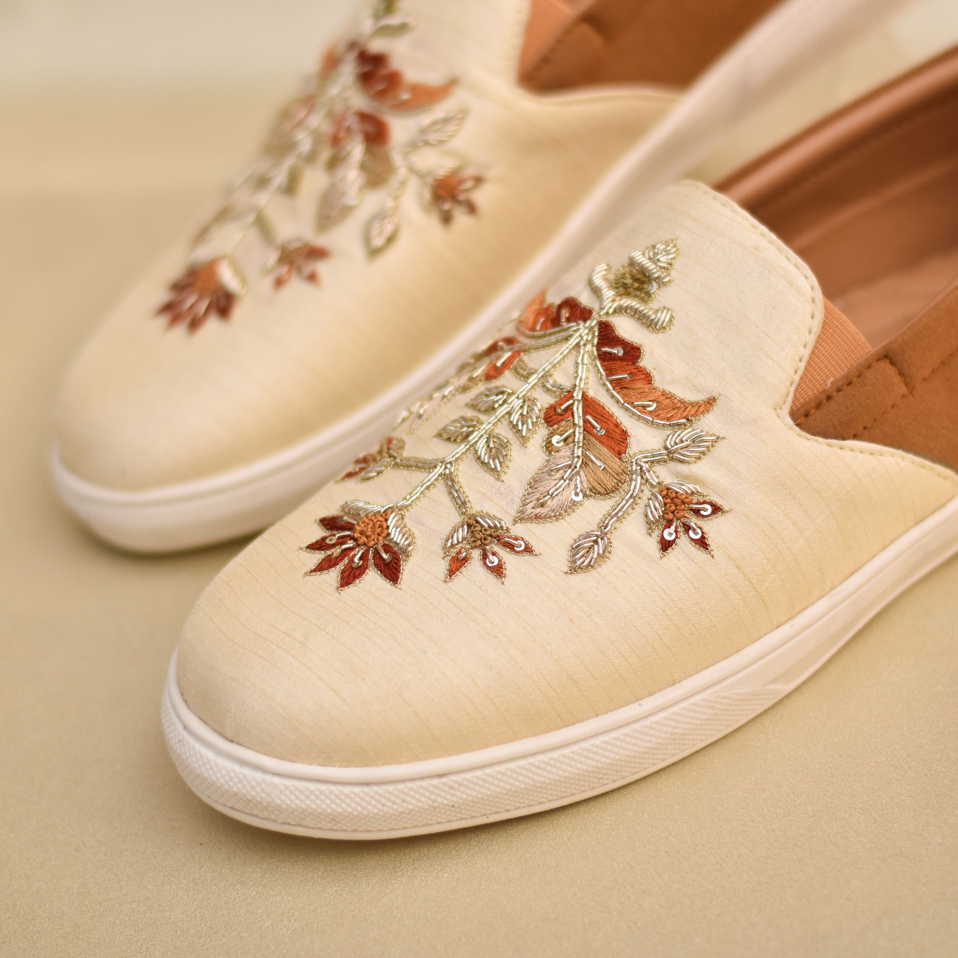 Embroidered festive shoes for grooms featuring floral patterns on ivory fabric and tan counter