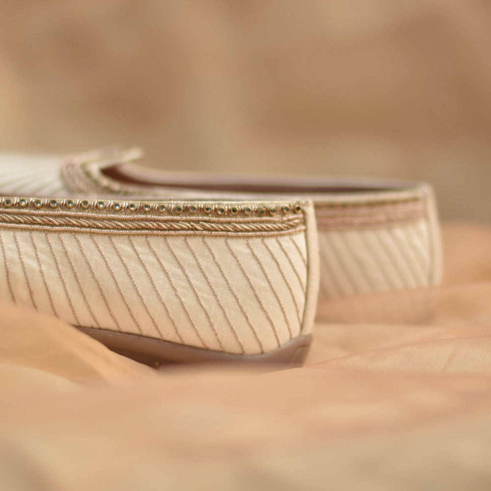 Ivory mojri with fine diagonal thread embroidery, detailed zari border, and delicate bead embellishments along the edge on a silk-textured base