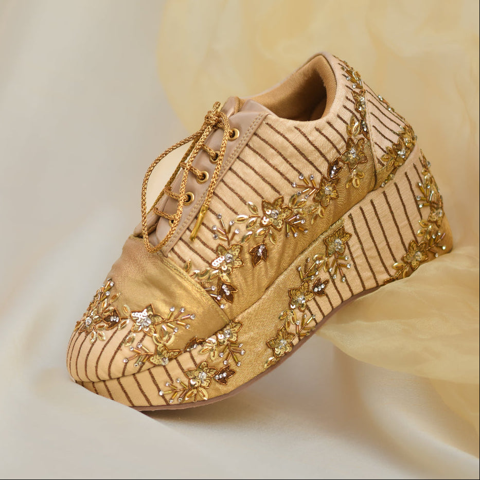 Gold embellished sneakers with floral detailing and striped pattern design