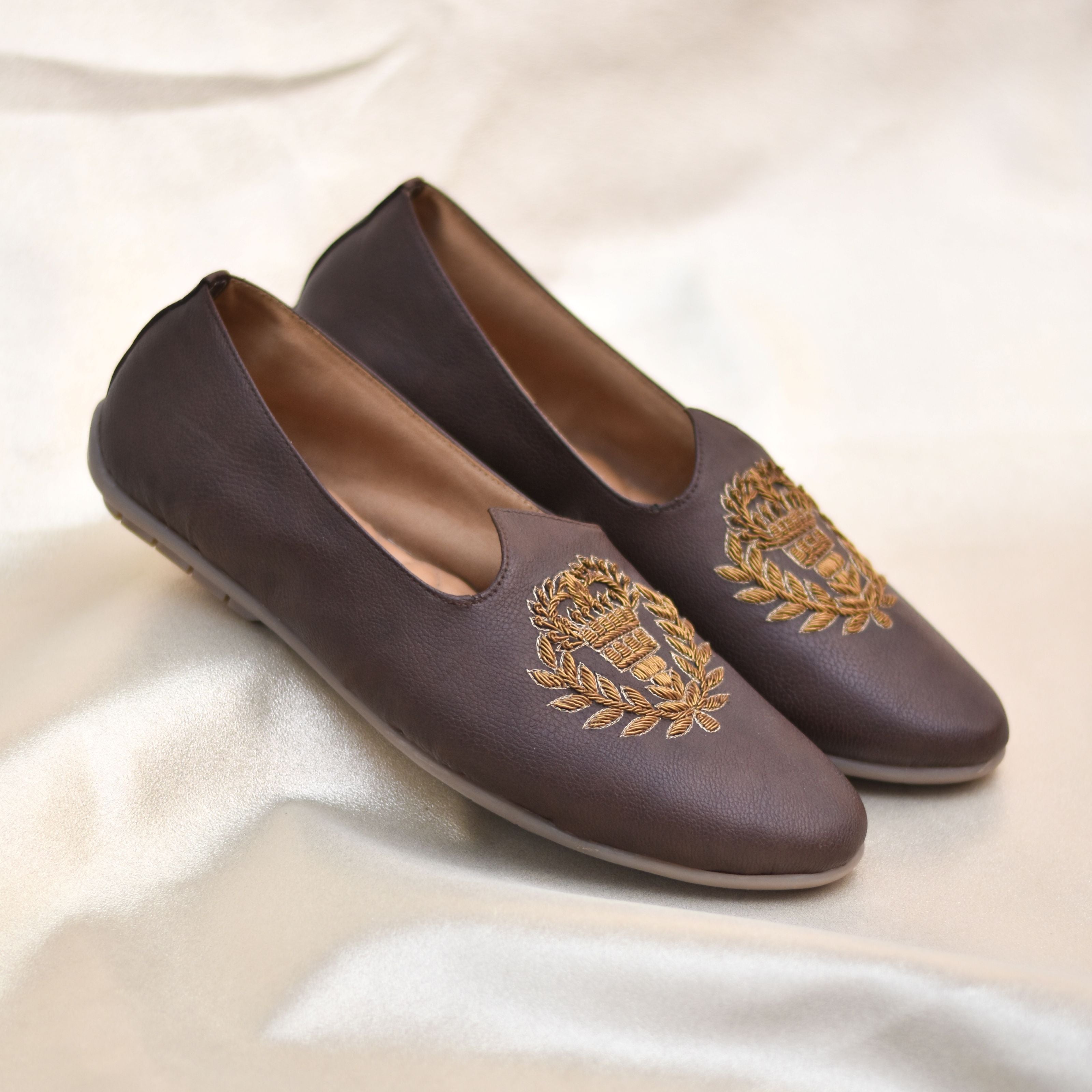 Traditional slip-on footwear in dark chocolate tone featuring royal insignia motif.