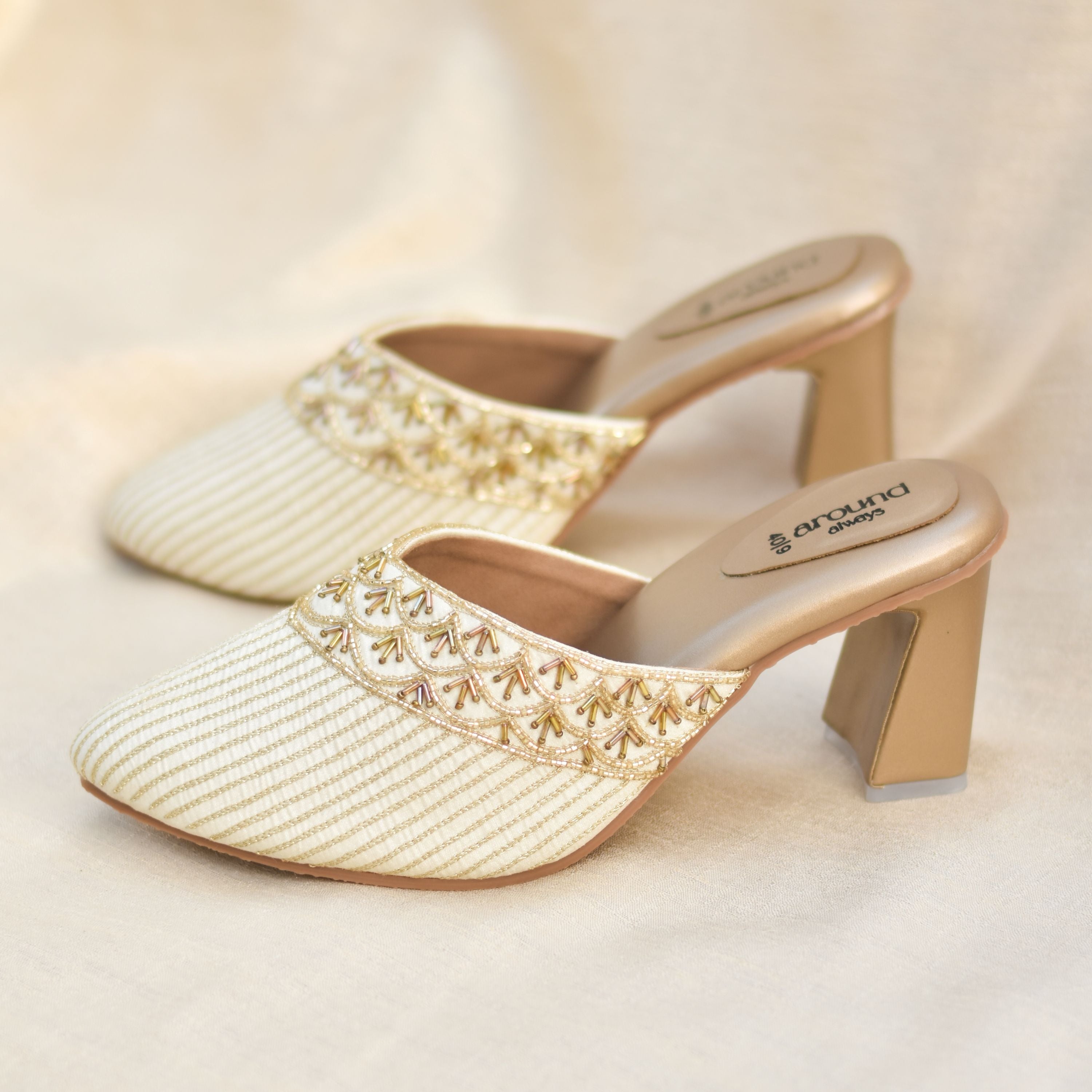 Ivory mule heels with golden stripes and beaded detailing.