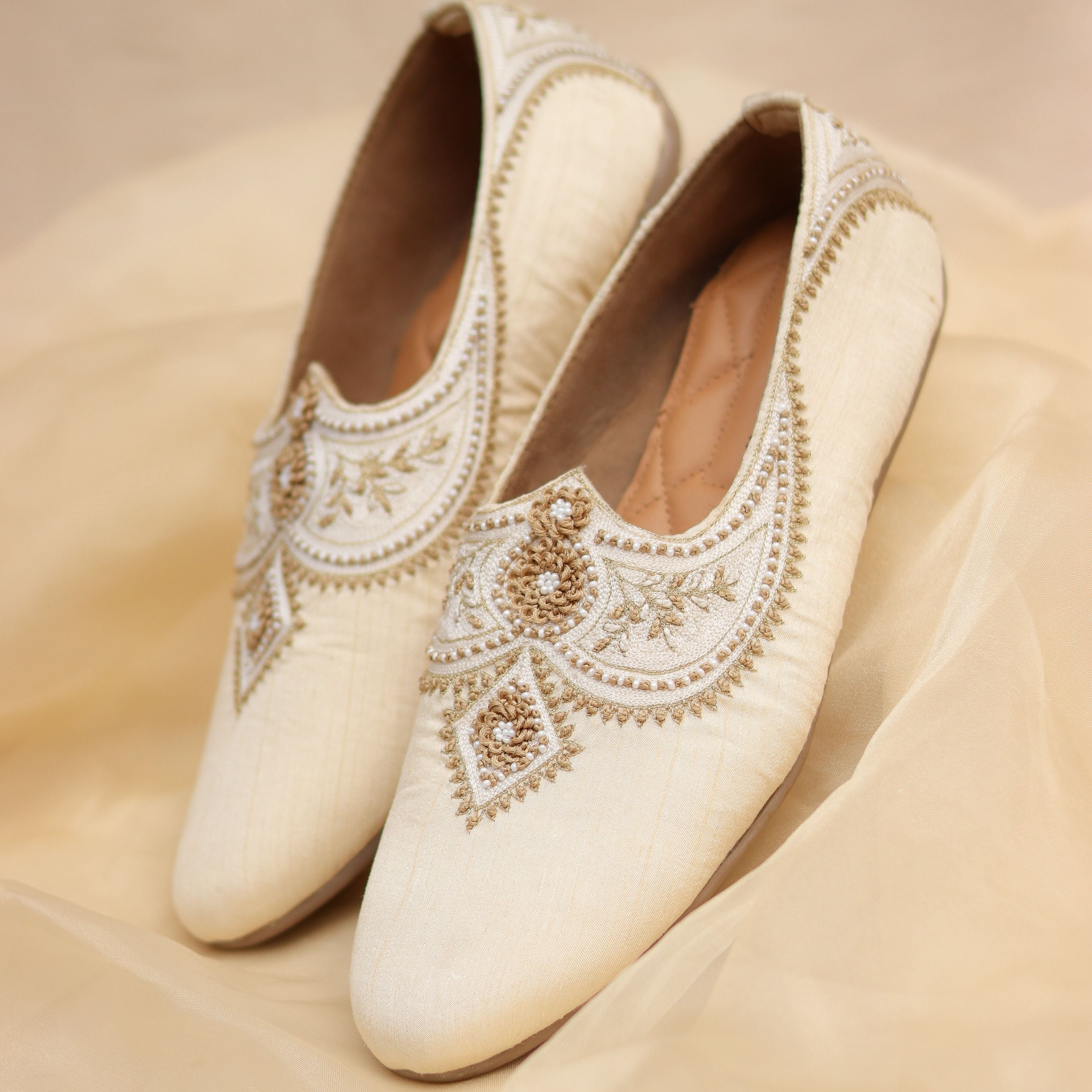Cream-colored groom footwear with intricate threadwork and beaded design.