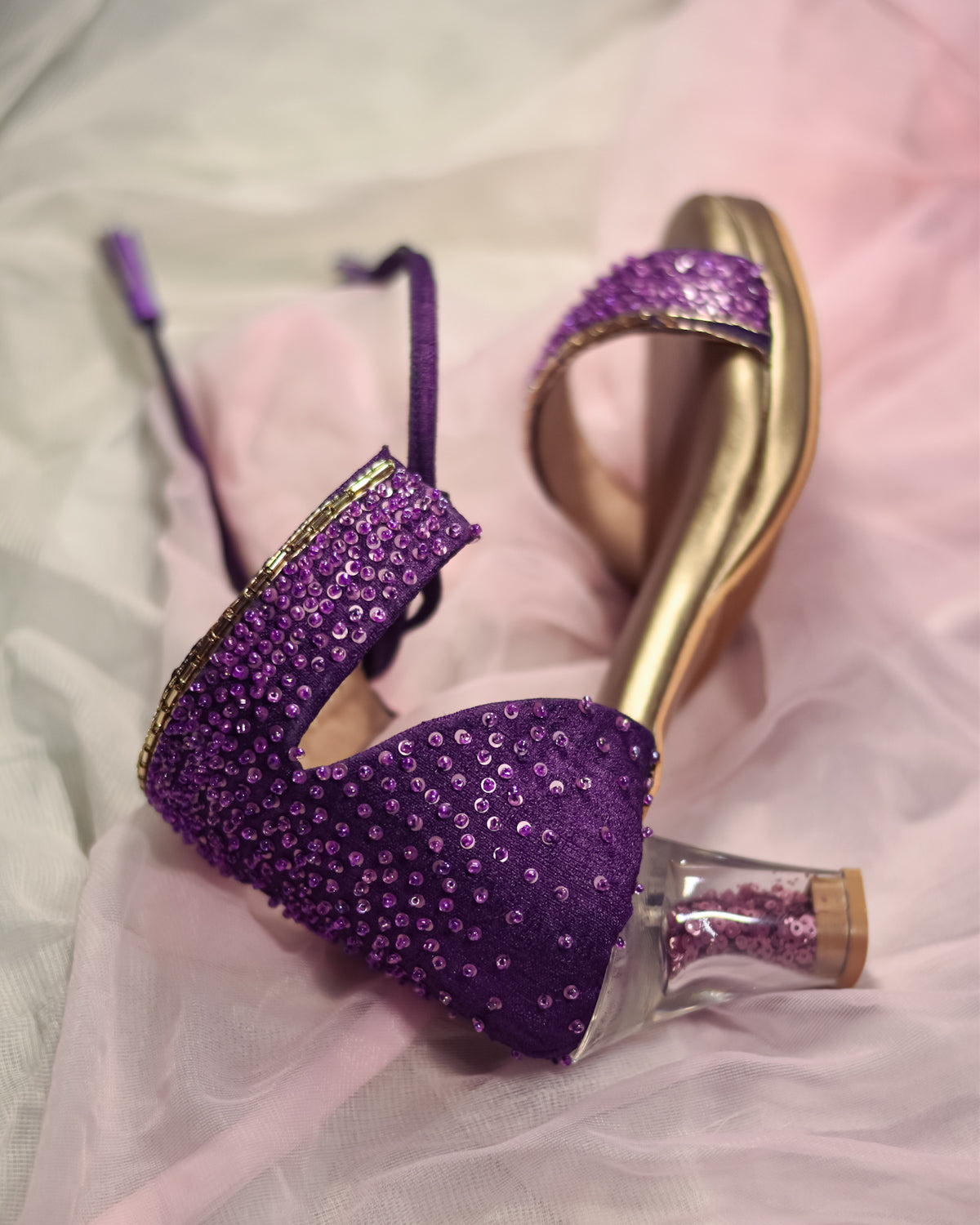 Purple high-heeled shoes with gold accents on a soft pink background