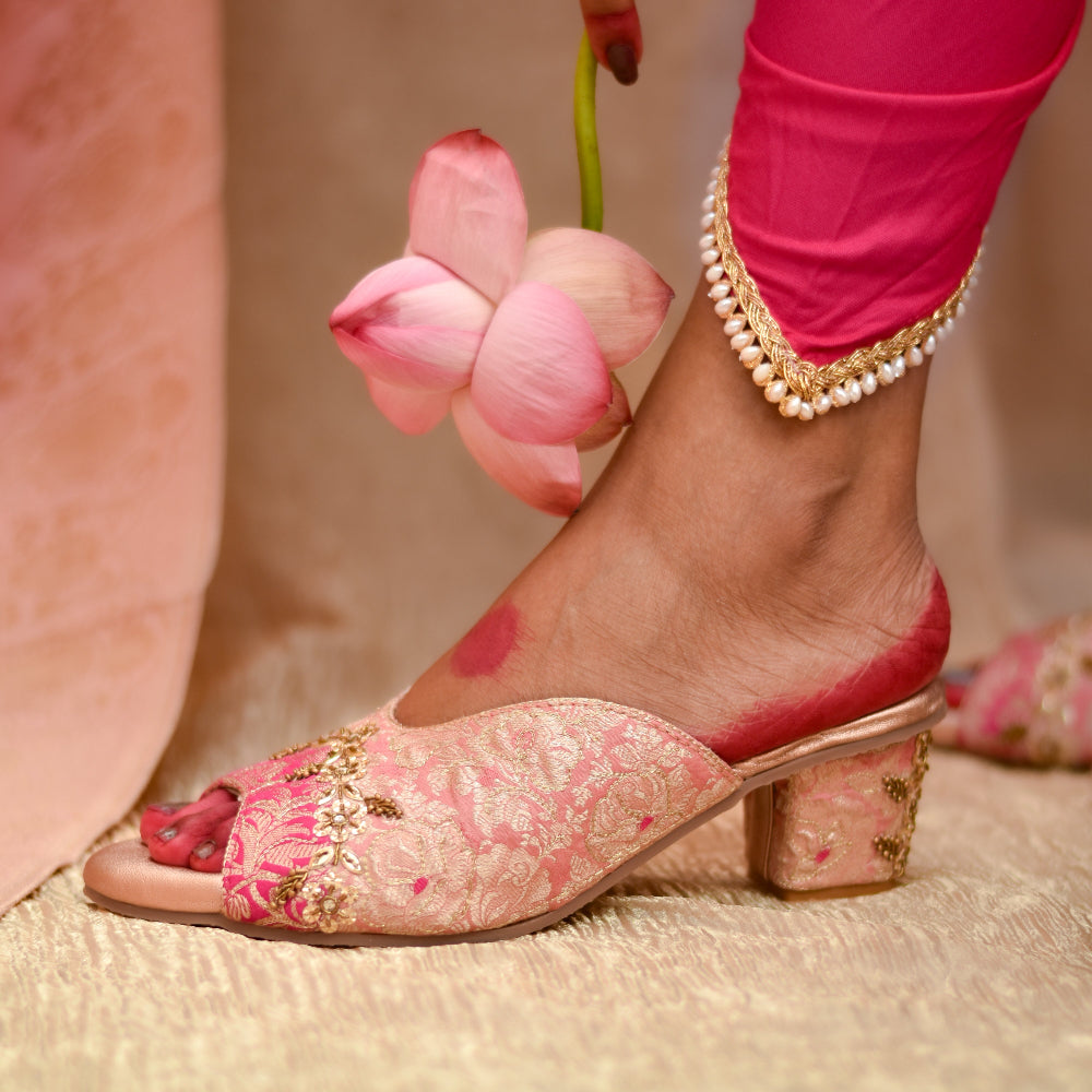 Embroidered pink sandal with gold details and stable heels worn by a person