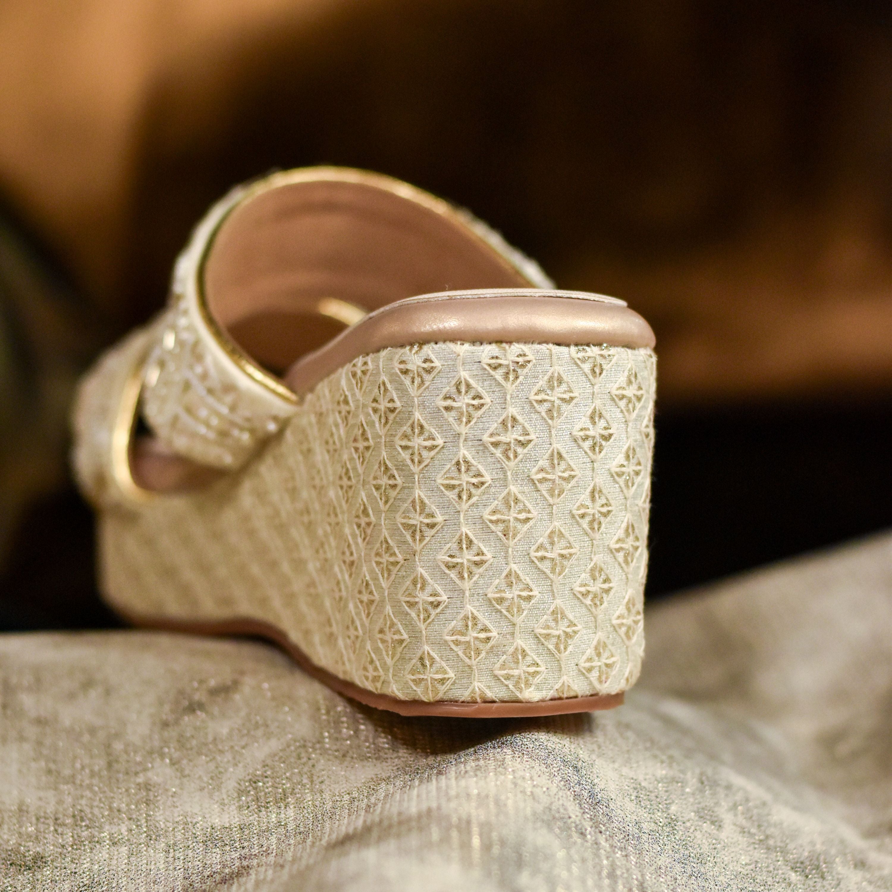 Stylish champagne gold wedge sandals with festive strap design.