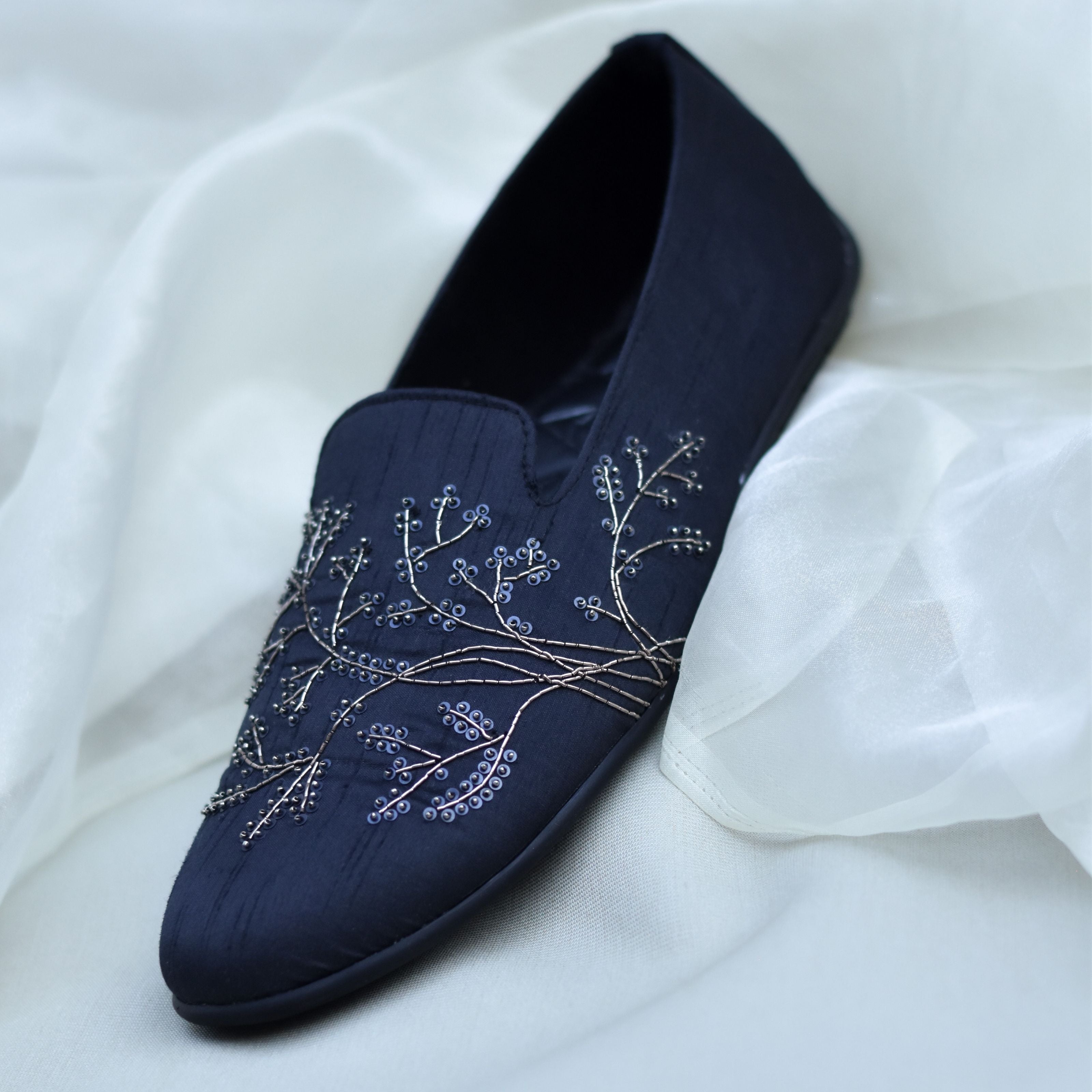 Ethnic slip-on shoes in black colour featuring branch-like stitched patterns.