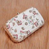 Angled view of the Mahika floral clutch on peach fabric