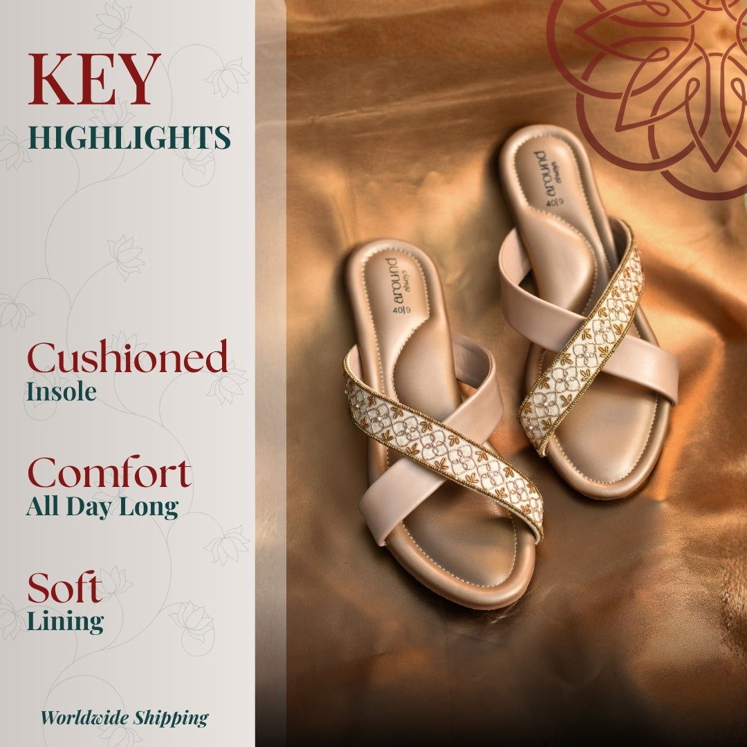 Beige embroidered crossover sandals with cushioned footbed placed on a glossy satin gold surface