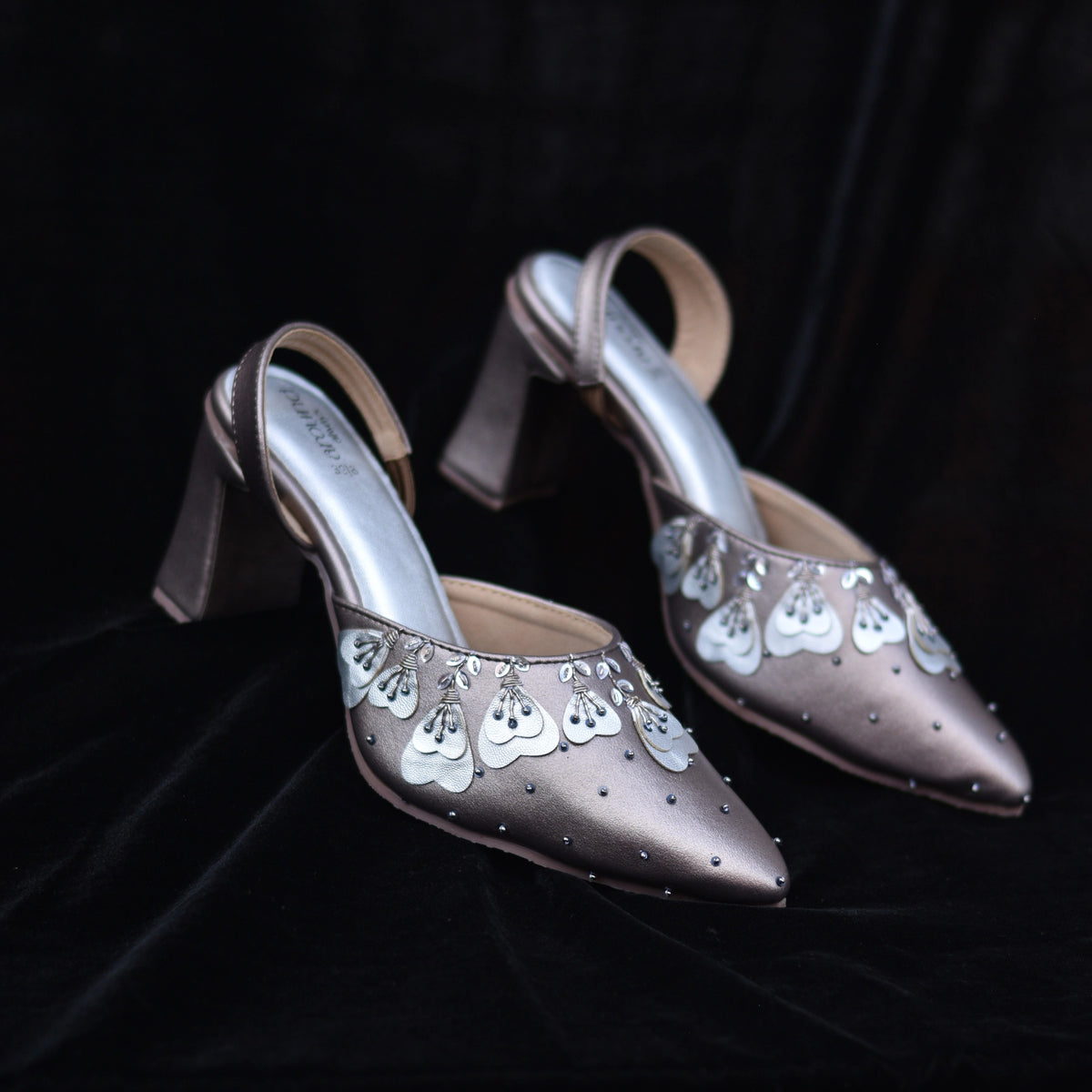 Pair of gunmetal slingback mules with petal embroidery on black background