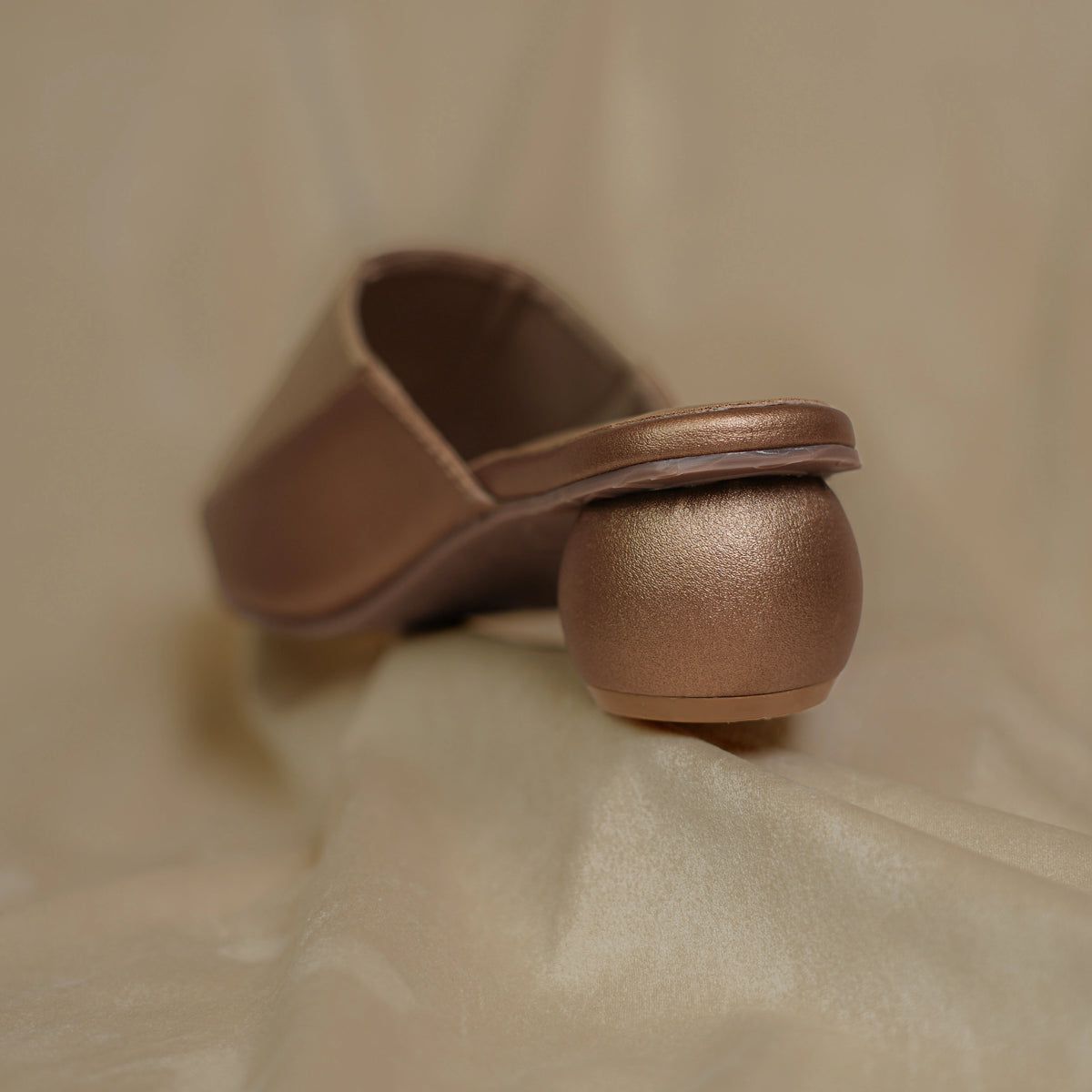 Close up of copper ball heel on metallic slip on mules